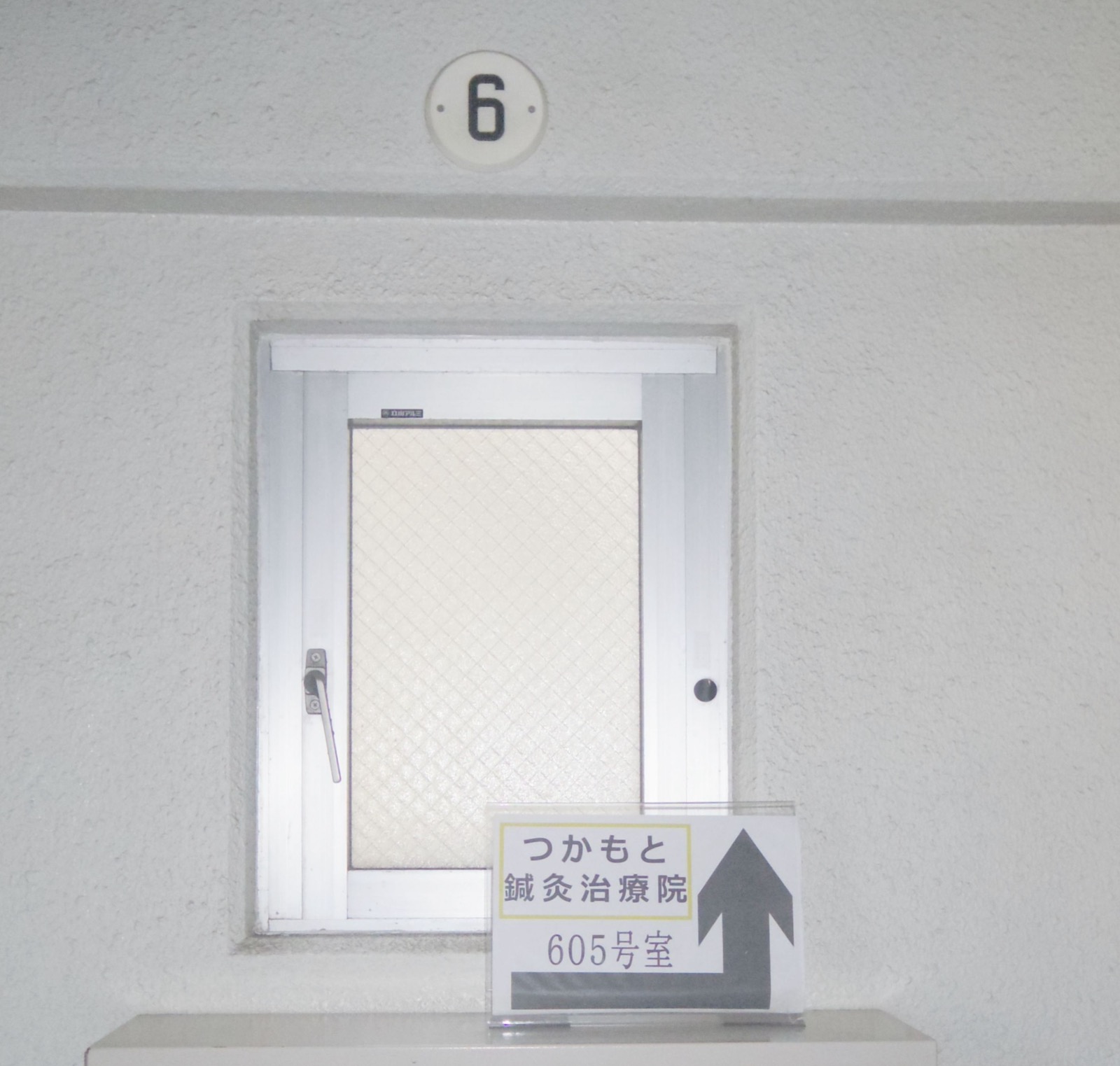 6階の壁にある階数表示と、つかもと鍼灸治療院 605号室への矢印付き案内板