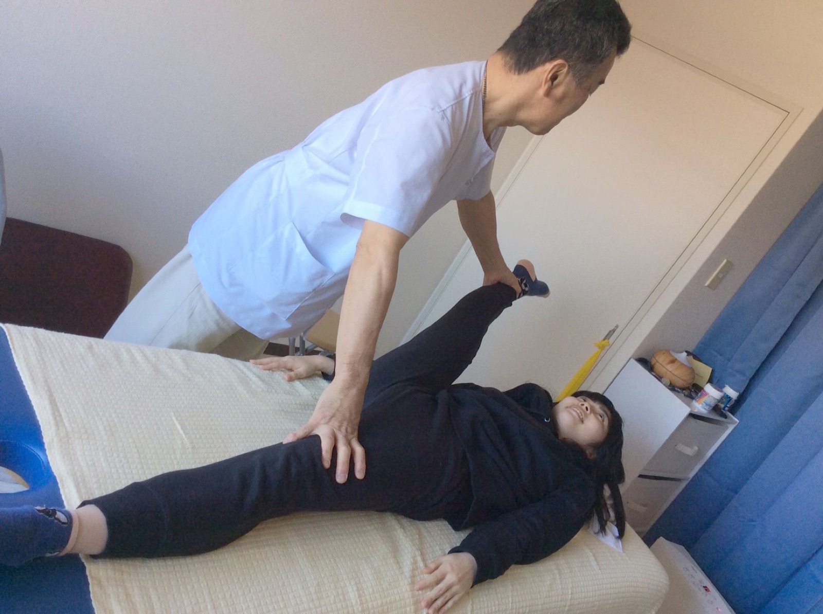 院長が施術ベッドで患者さんの脚を伸ばしながら施術している様子